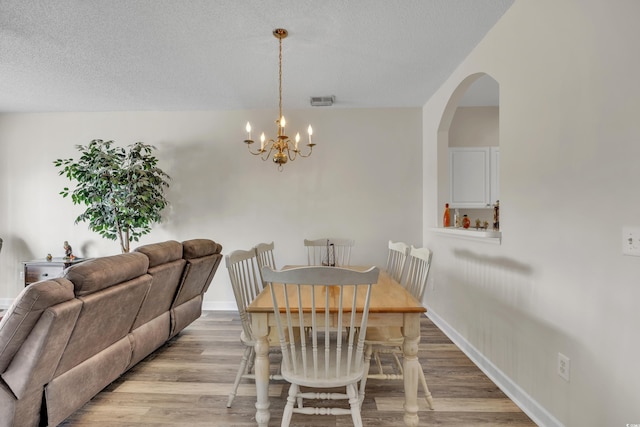 dining area featuring light wood-style flooring, a chandelier, visible vents, and a textured ceiling