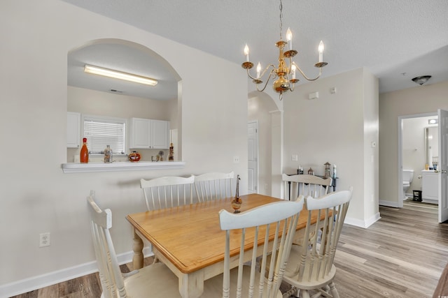 dining room featuring a textured ceiling, baseboards, arched walkways, and light wood-type flooring