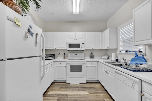 kitchen with a sink, white cabinets, light countertops, and white appliances