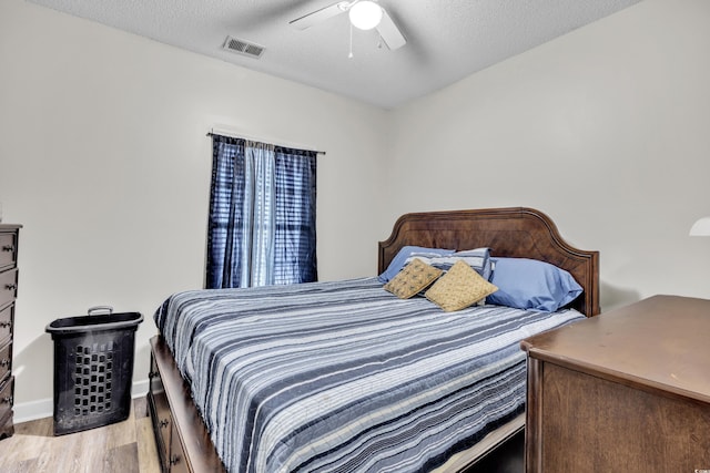 bedroom with light wood-style flooring, a textured ceiling, a ceiling fan, and visible vents