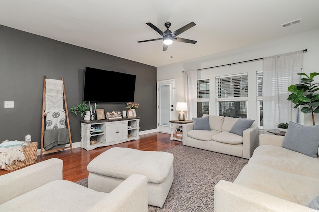 living area with dark wood-type flooring, visible vents, baseboards, and a ceiling fan