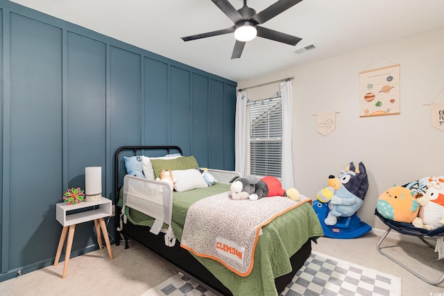 bedroom featuring light colored carpet, a decorative wall, visible vents, and ceiling fan