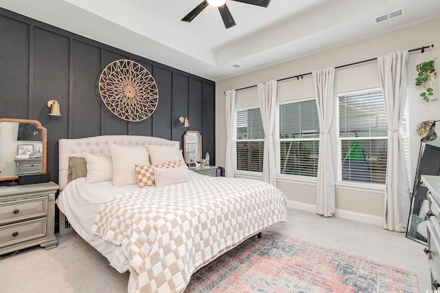 bedroom with a raised ceiling, visible vents, a decorative wall, light carpet, and baseboards