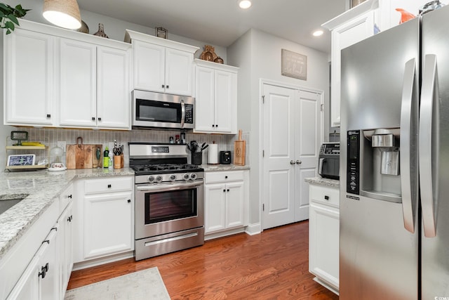 kitchen featuring appliances with stainless steel finishes, white cabinetry, decorative backsplash, and wood finished floors