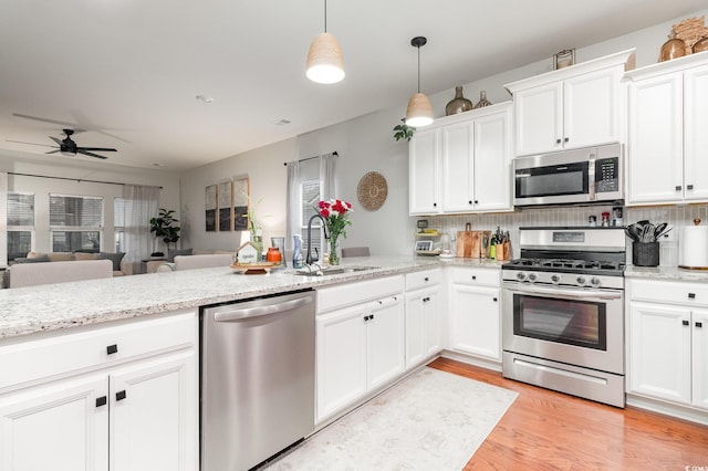 kitchen featuring white cabinets, open floor plan, hanging light fixtures, appliances with stainless steel finishes, and light wood finished floors