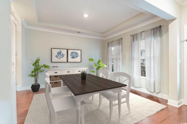 dining space featuring ornamental molding, wood finished floors, a raised ceiling, and baseboards