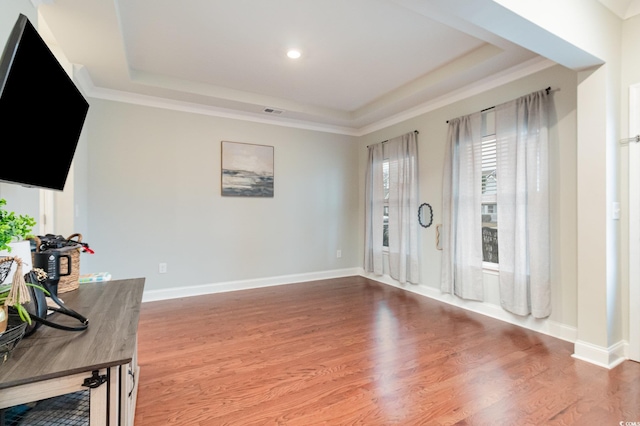 interior space with crown molding, a tray ceiling, wood finished floors, and baseboards