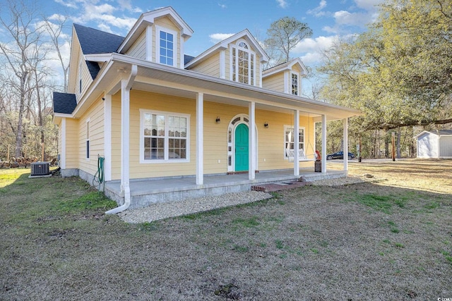 view of front of home with a shingled roof, a front yard, covered porch, and central AC unit