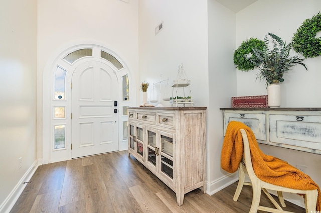 entryway with a towering ceiling, baseboards, wood finished floors, and visible vents