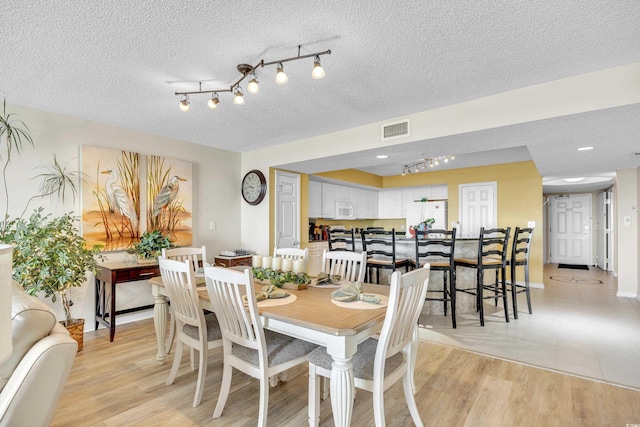 dining room featuring baseboards, visible vents, a textured ceiling, and light wood finished floors