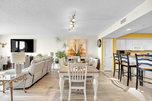 dining area with light wood-type flooring, visible vents, and a textured ceiling