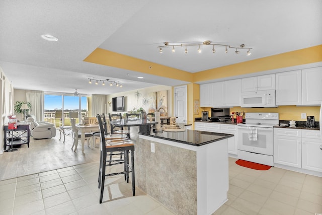 kitchen with white appliances, a kitchen breakfast bar, open floor plan, white cabinets, and dark countertops