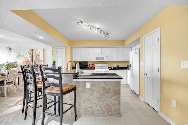 kitchen featuring white appliances, dark countertops, a breakfast bar, and white cabinets