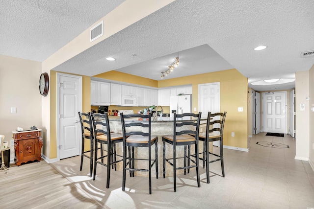 kitchen featuring visible vents, white cabinets, a kitchen breakfast bar, white appliances, and baseboards