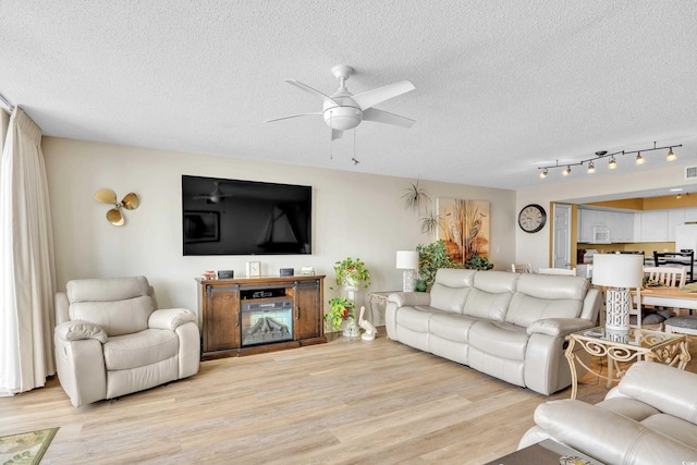 living room with light wood-style floors, ceiling fan, and a textured ceiling