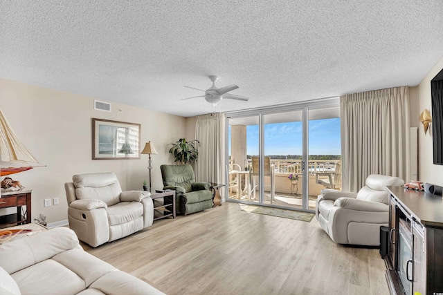 living room featuring light wood-style floors, floor to ceiling windows, visible vents, and a textured ceiling