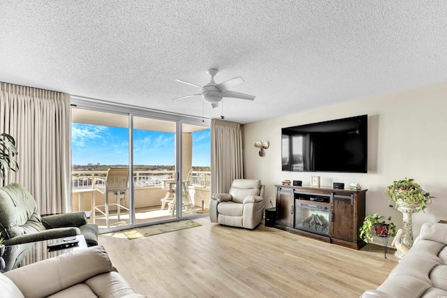 living room with a textured ceiling, a wall of windows, light wood-type flooring, and a ceiling fan