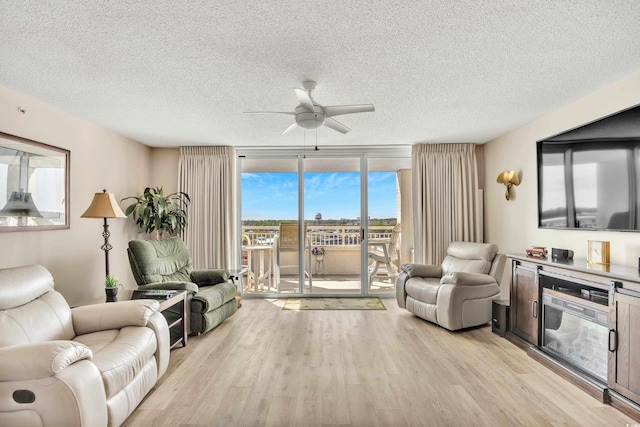 living area featuring a textured ceiling, ceiling fan, light wood finished floors, and a wall of windows