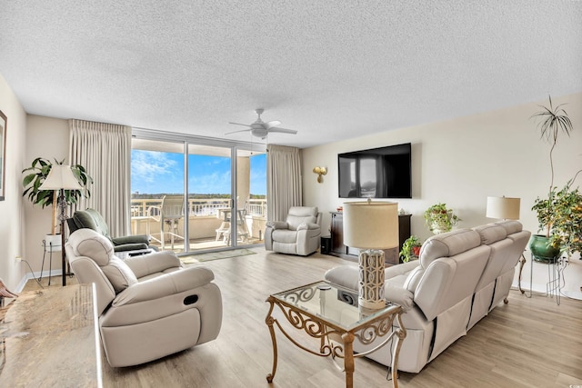 living room with a ceiling fan, floor to ceiling windows, a textured ceiling, and light wood finished floors