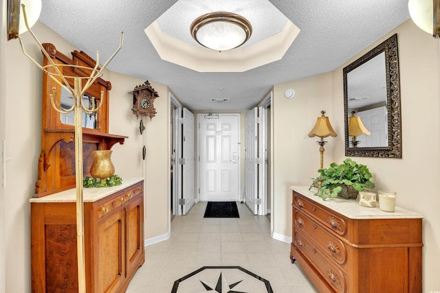 interior space featuring light tile patterned floors, baseboards, a raised ceiling, and a textured ceiling