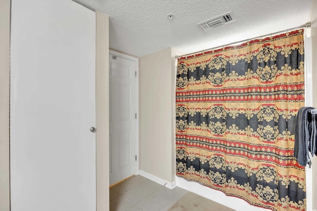 full bath featuring visible vents, a shower with shower curtain, a textured ceiling, baseboards, and tile patterned floors