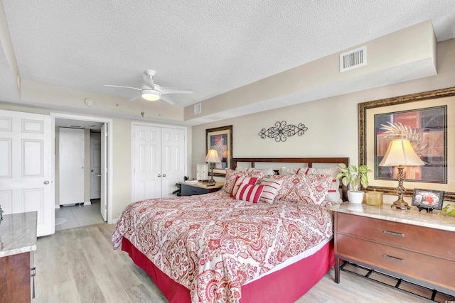 bedroom with a textured ceiling, light wood-style flooring, a closet, and visible vents