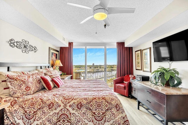 bedroom with a textured ceiling, a ceiling fan, access to exterior, light wood-type flooring, and floor to ceiling windows