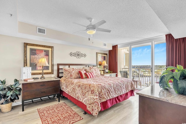 bedroom featuring light wood-type flooring, a water view, visible vents, and access to exterior