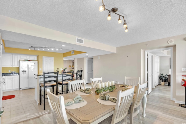 dining space with light wood-style flooring, visible vents, and a textured ceiling