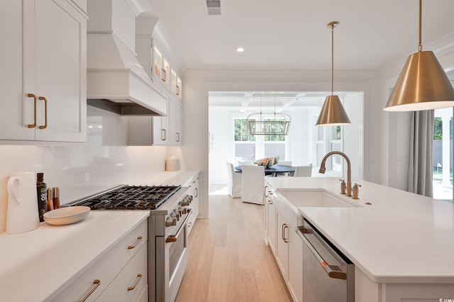 kitchen with premium range hood, a sink, white cabinets, appliances with stainless steel finishes, and decorative light fixtures