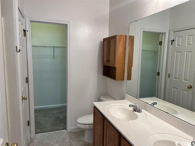 full bath with toilet, a sink, tile patterned floors, double vanity, and a walk in closet