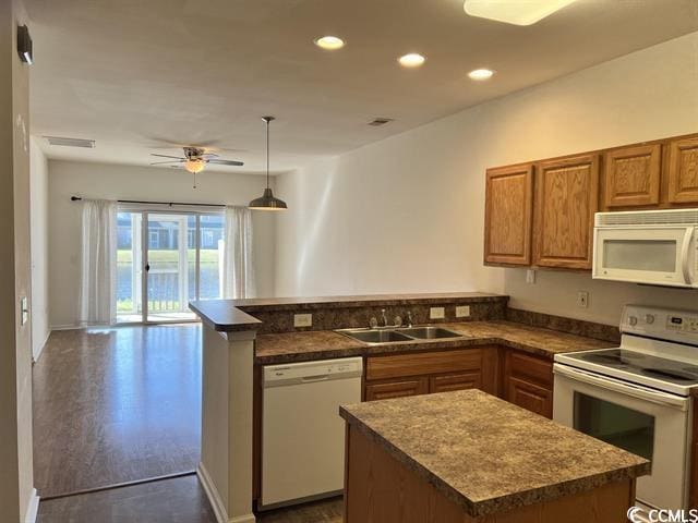 kitchen featuring white appliances, dark countertops, brown cabinets, a peninsula, and a sink