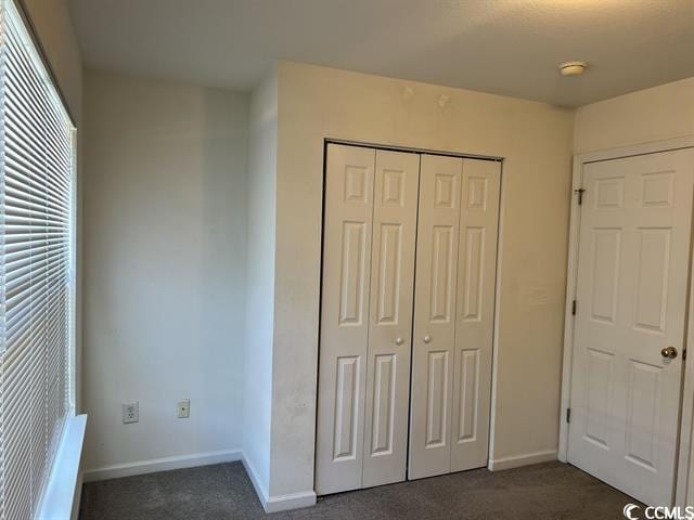 unfurnished bedroom featuring a closet, dark carpet, and baseboards