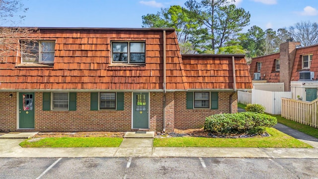 view of property with mansard roof, fence, uncovered parking, central AC, and brick siding