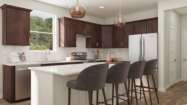 kitchen featuring a sink, a kitchen island, light countertops, appliances with stainless steel finishes, and hanging light fixtures