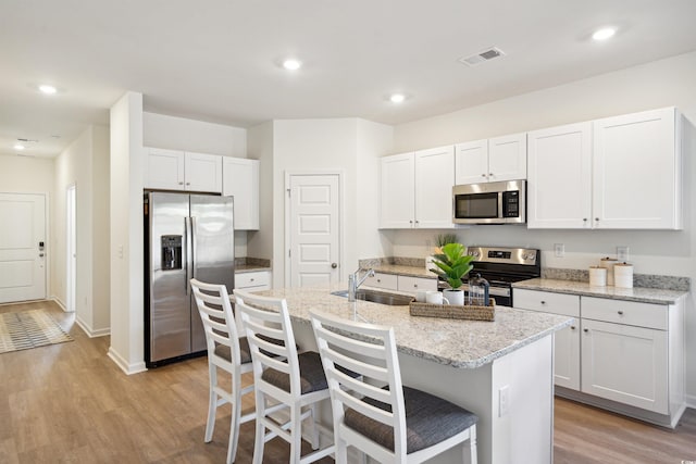 kitchen featuring visible vents, an island with sink, stainless steel appliances, white cabinetry, and a sink