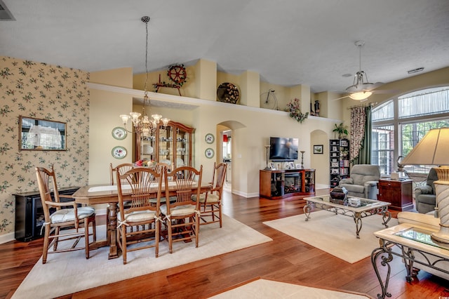 dining area featuring wallpapered walls, arched walkways, baseboards, wood finished floors, and a notable chandelier