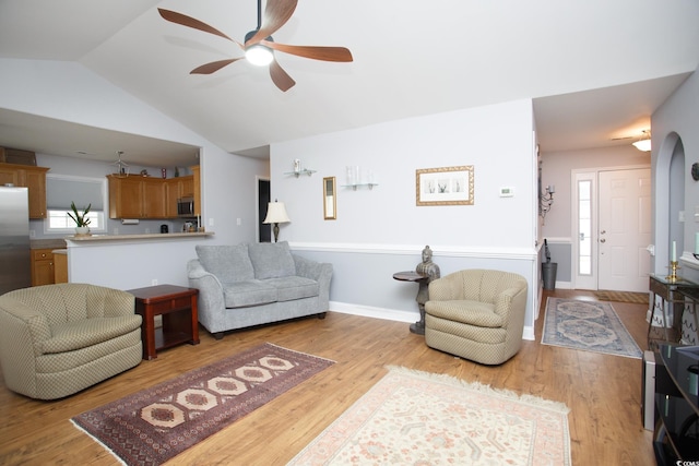 living room with lofted ceiling, light wood-type flooring, a ceiling fan, and baseboards