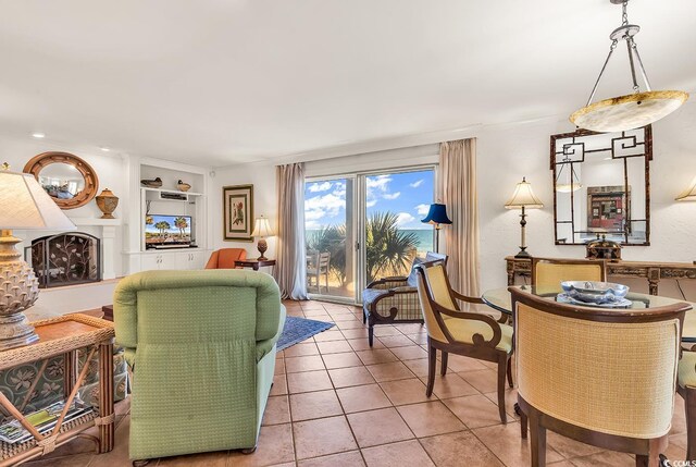 living area featuring a fireplace with raised hearth, built in shelves, and light tile patterned flooring