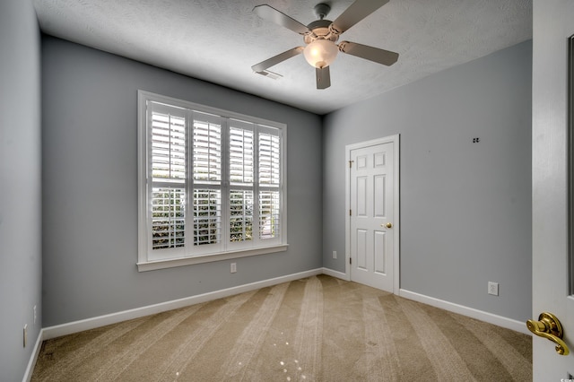 empty room featuring a textured ceiling, carpet floors, ceiling fan, and baseboards