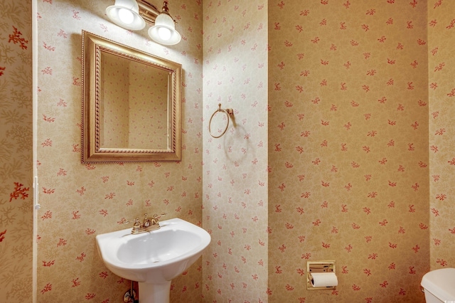 bathroom featuring toilet, wallpapered walls, and a sink