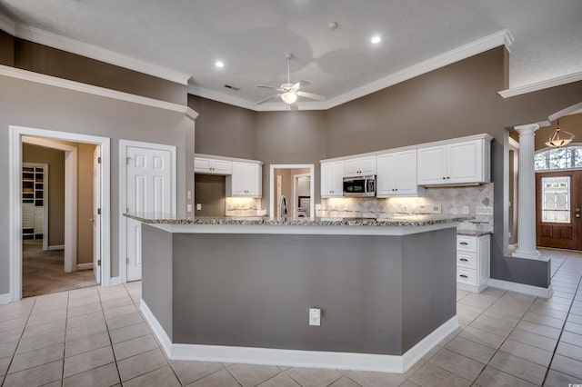 kitchen with a ceiling fan, light stone countertops, ornate columns, stainless steel microwave, and crown molding