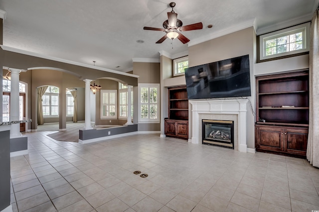 unfurnished living room featuring a healthy amount of sunlight, ornate columns, a fireplace, and arched walkways