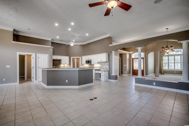 kitchen featuring arched walkways, light tile patterned floors, stainless steel microwave, ornate columns, and ceiling fan with notable chandelier