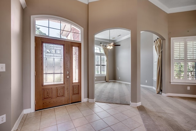 entrance foyer featuring crown molding, light tile patterned floors, light colored carpet, a high ceiling, and baseboards