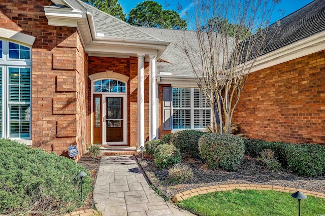 view of exterior entry featuring a shingled roof and brick siding