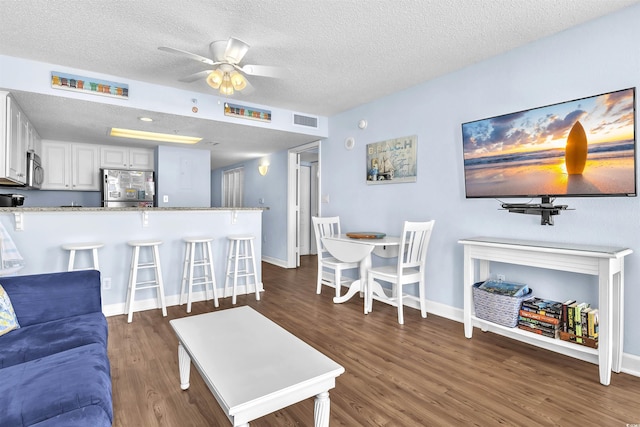 living area featuring a textured ceiling, dark wood-style flooring, baseboards, visible vents, and ceiling fan