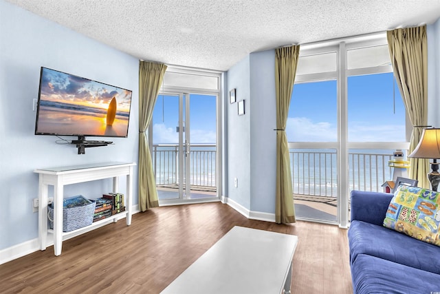 living area with a textured ceiling, a water view, baseboards, wood finished floors, and floor to ceiling windows