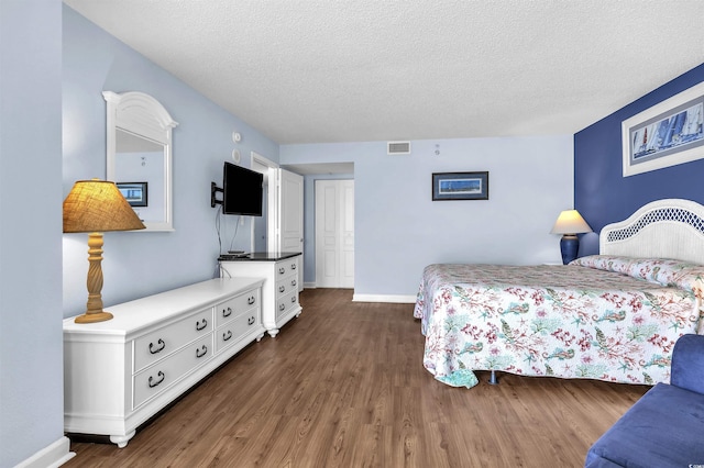bedroom with baseboards, wood finished floors, visible vents, and a textured ceiling