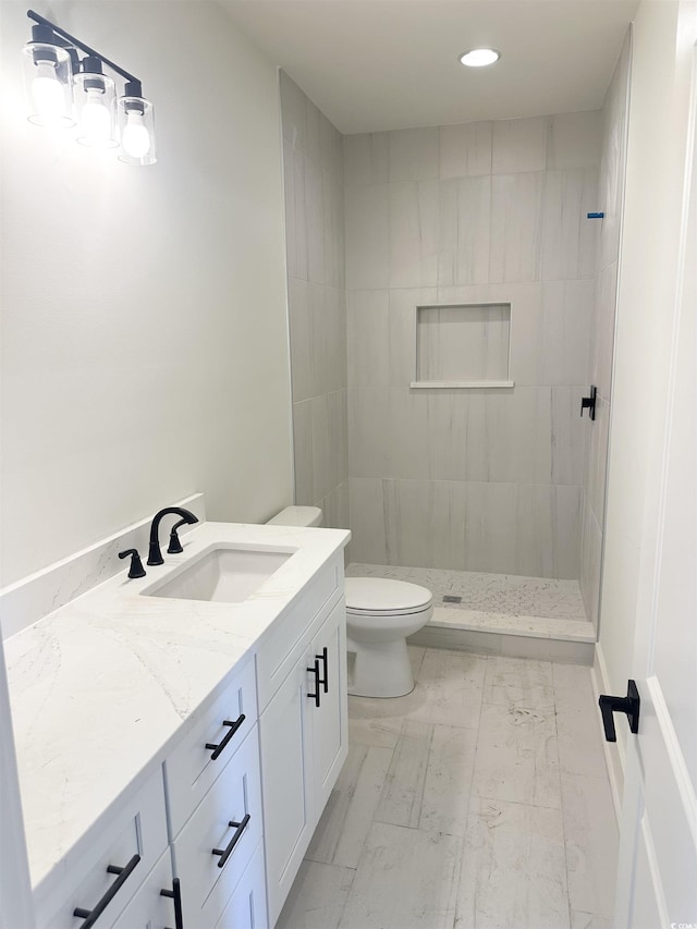 bathroom with marble finish floor, a tile shower, vanity, and toilet